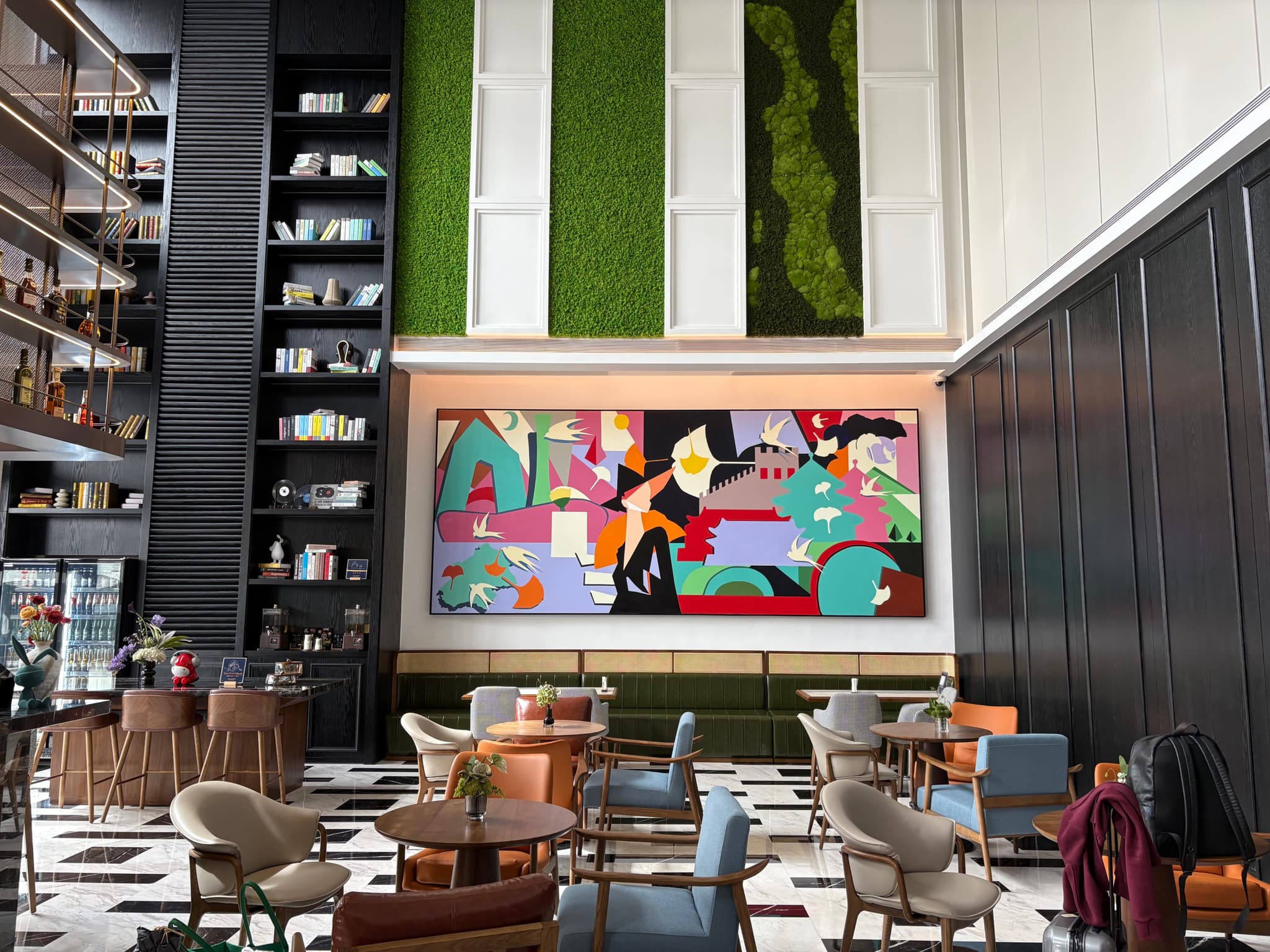 A modern lounge area with colorful abstract artwork, vertical green wall panels, high ceilings, and stylish seating arrangements