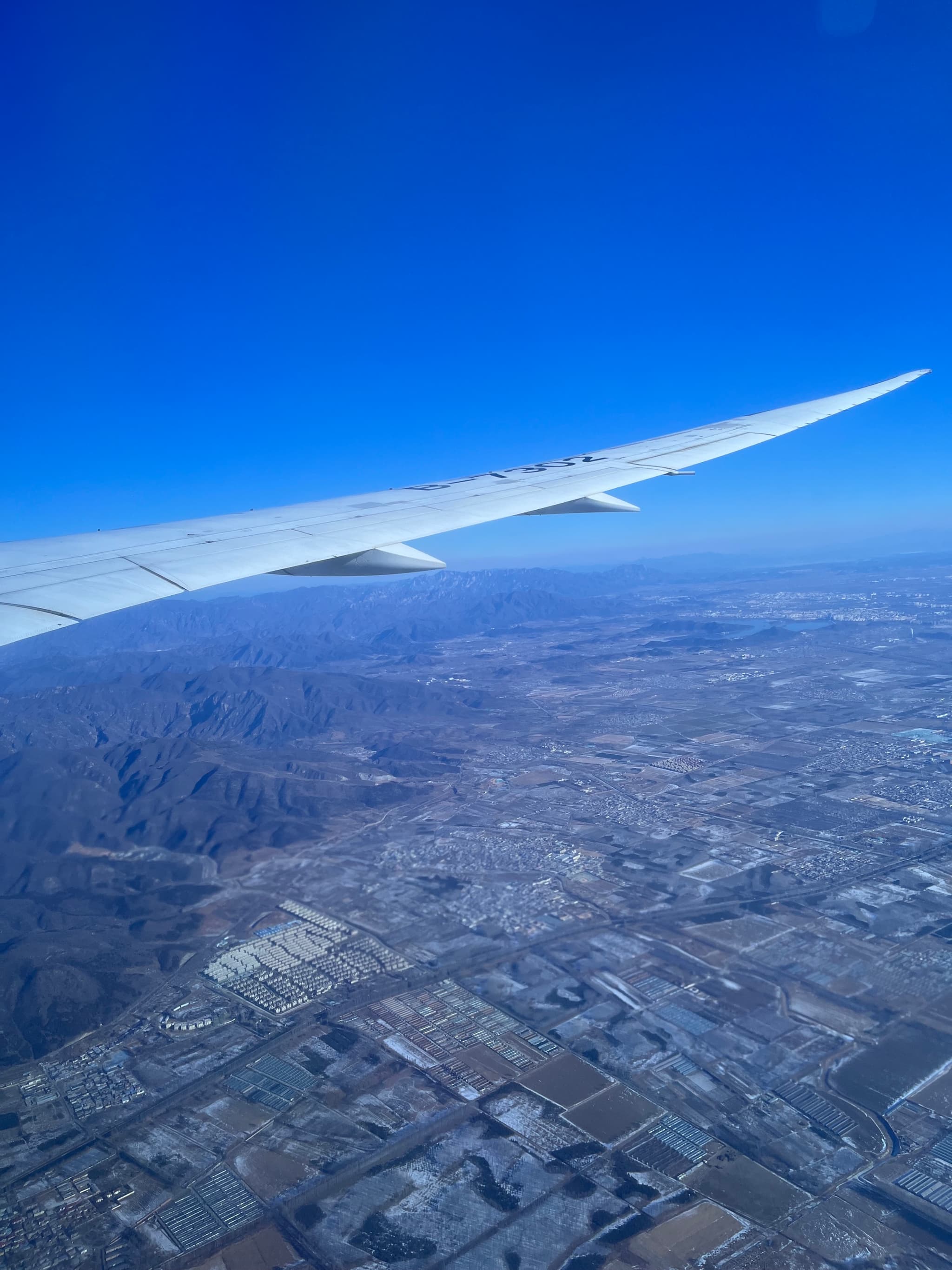 An airplane wing in flight with a view of a cityscape and fields below under a clear blue sky