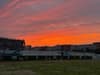 A vibrant sunset with orange and pink hues over a sports field and surrounding buildings