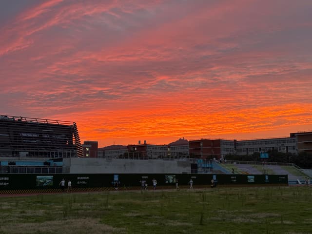 A vibrant sunset with orange and pink hues over a sports field and surrounding buildings