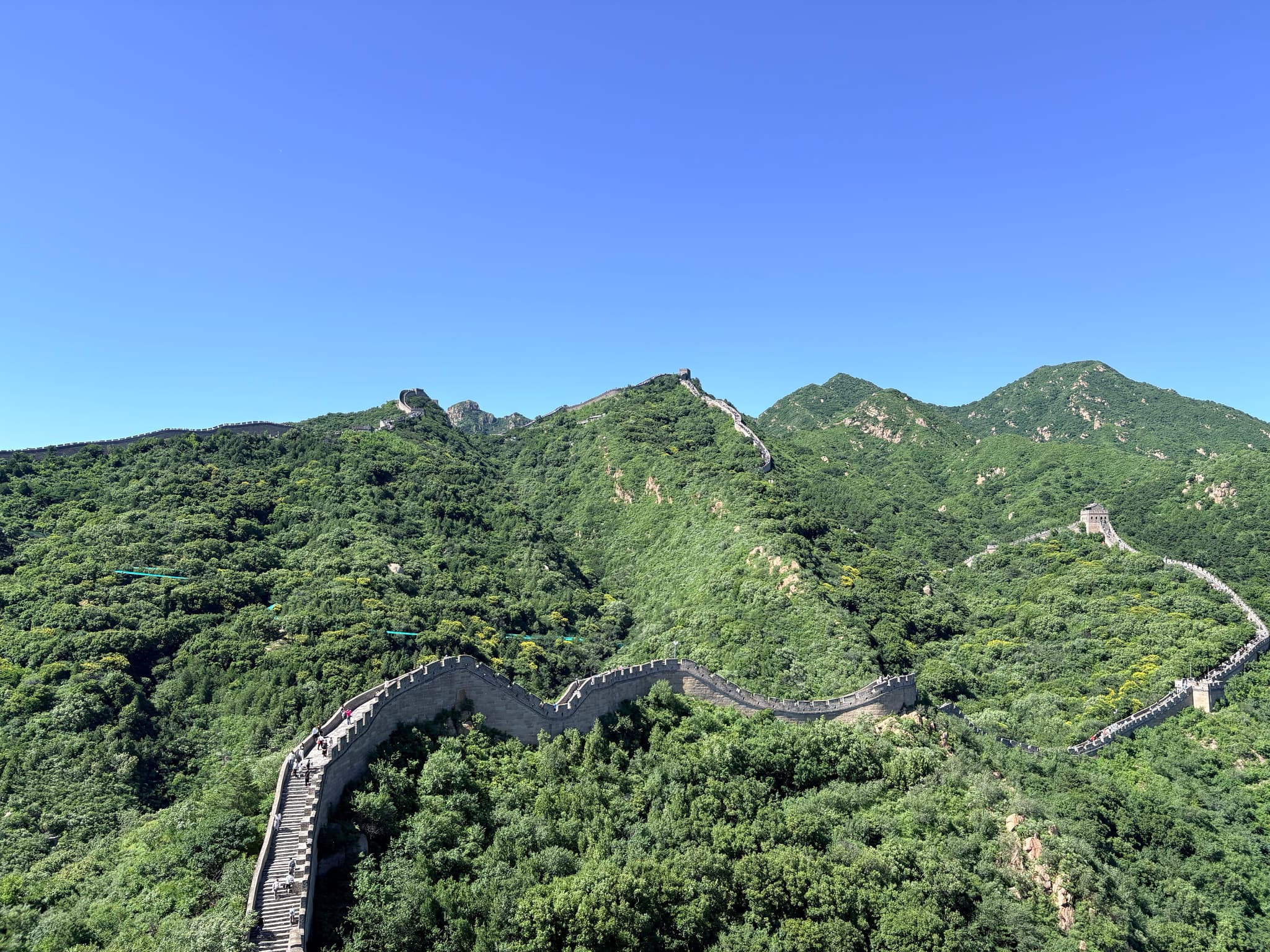Winding stone wall crossing forested mountain ridges beneath a clear blue sky