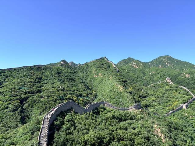 Winding stone wall crossing forested mountain ridges beneath a clear blue sky