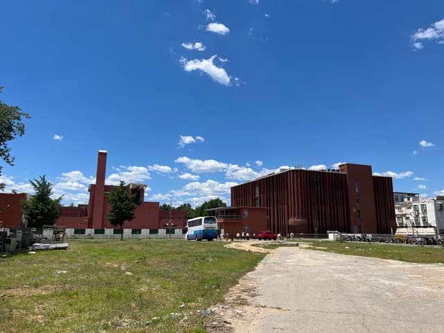 A large brick industrial building with a tall smokestack sits under a blue sky with scattered clouds