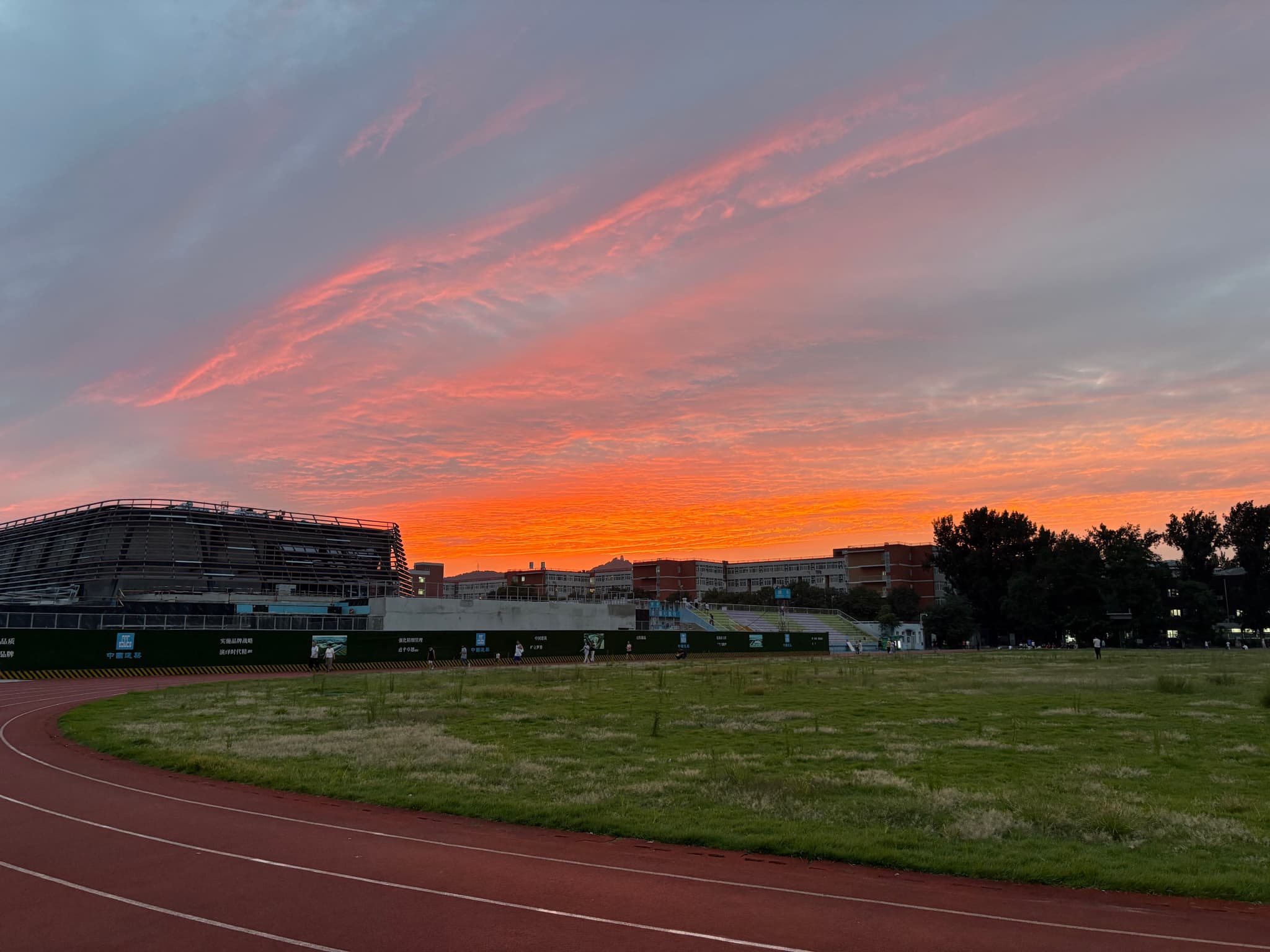 A vibrant sunrise paints the sky with orange and pink hues over a grassy field and buildings