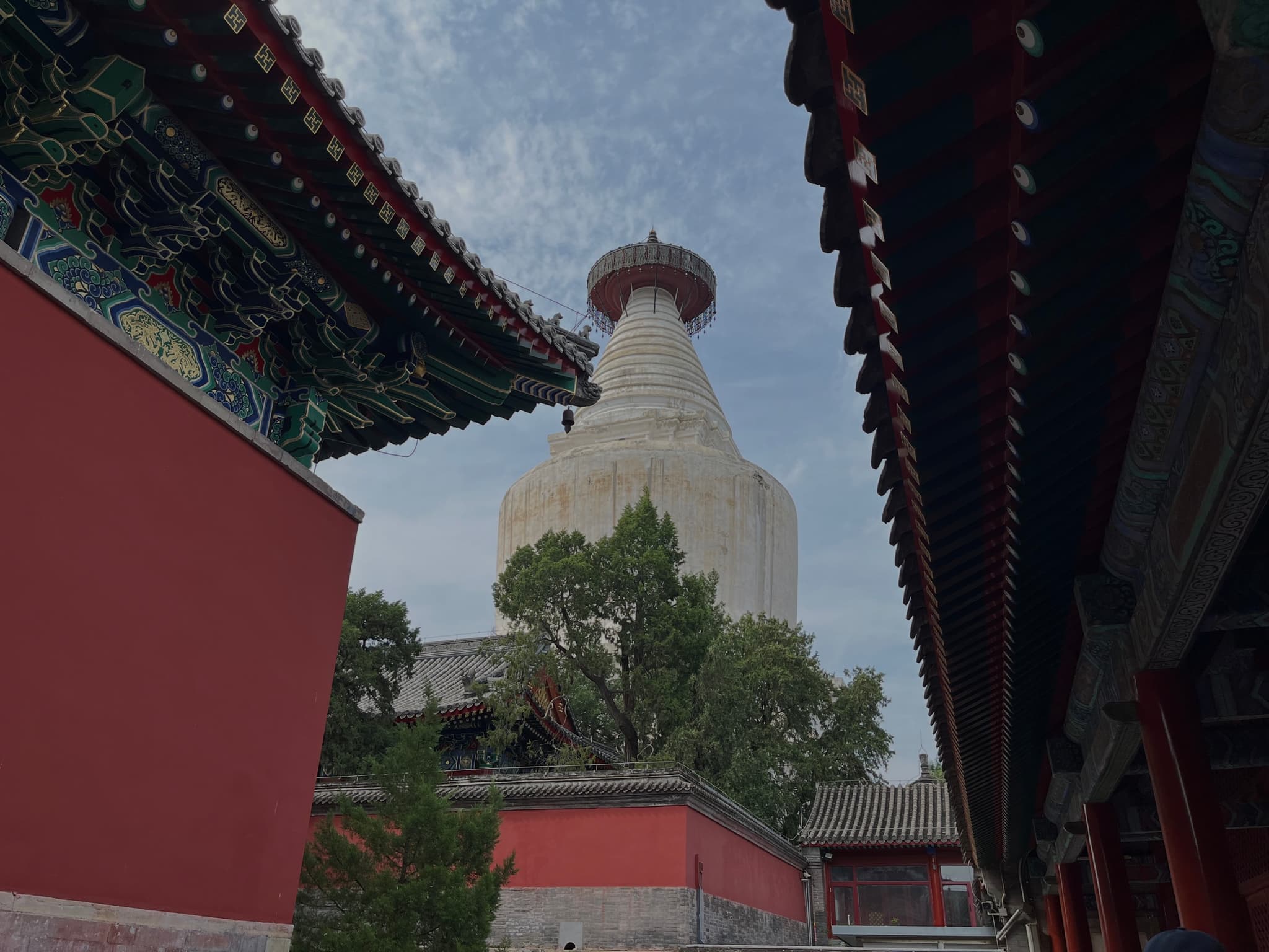 A white pagoda surrounded by traditional Chinese architecture and red walls under a partly cloudy sky