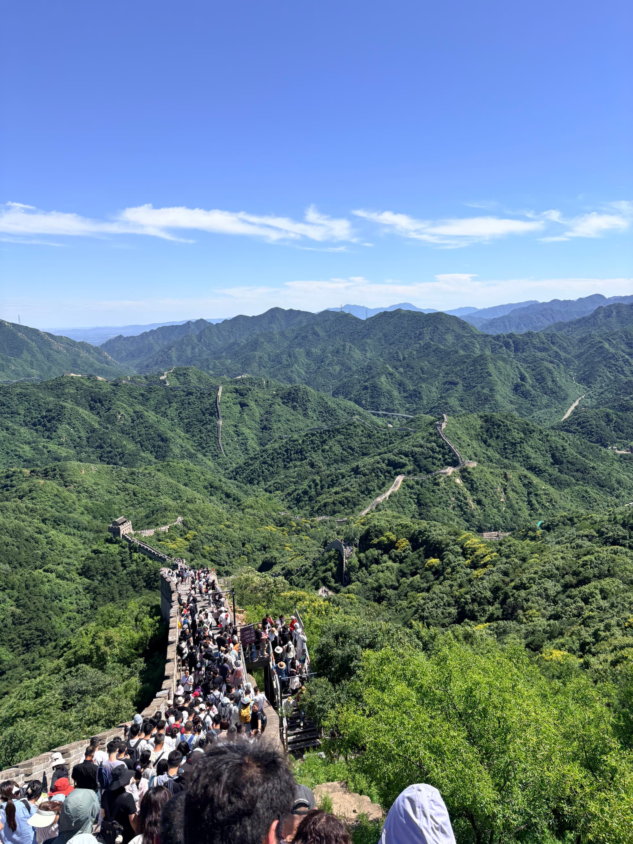 Great Wall winding across forested mountain ridges beneath a blue sky