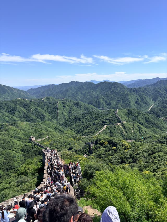 Great Wall winding across forested mountain ridges beneath a blue sky