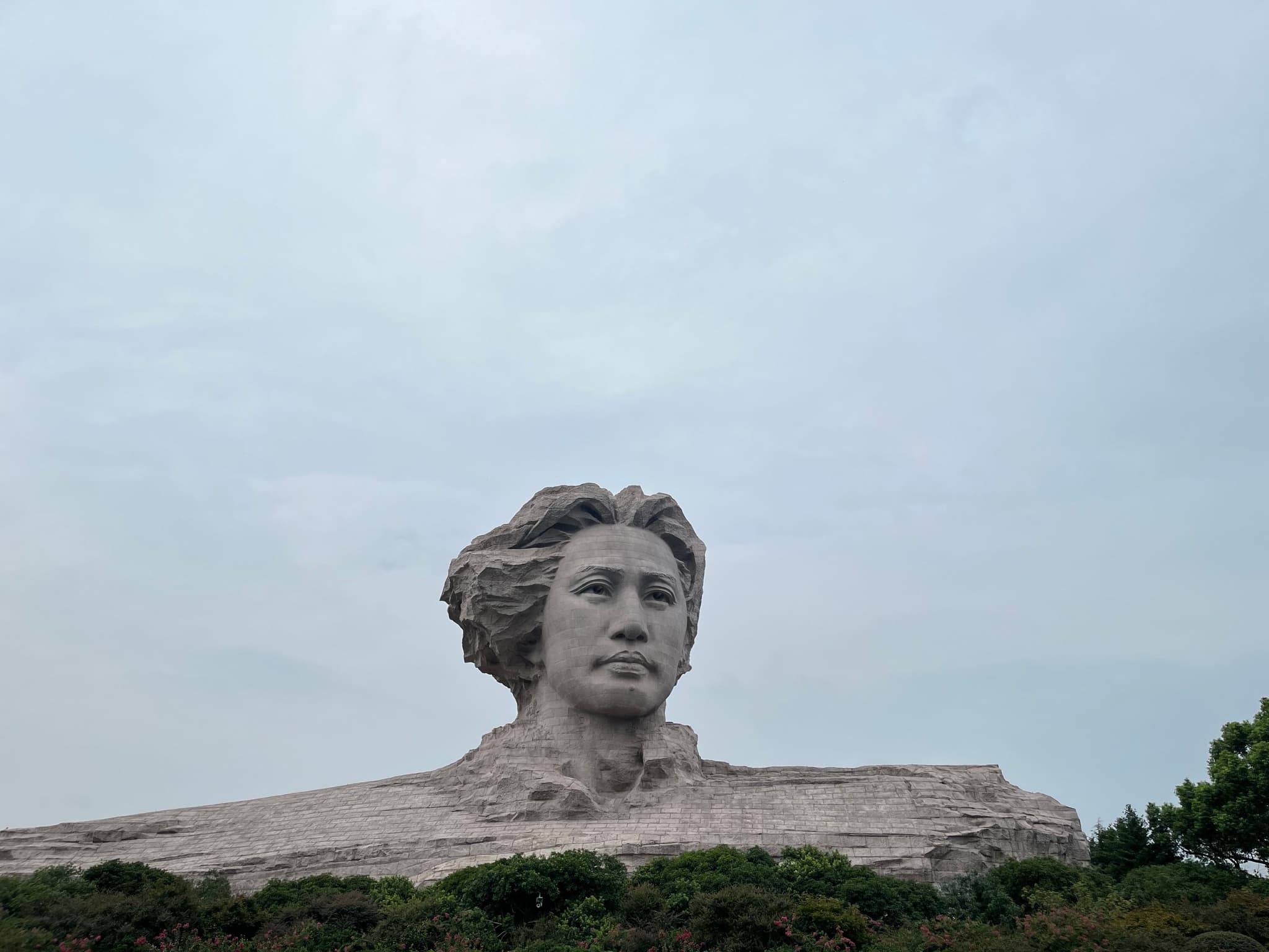 A rock formation resembling a human profile set against a cloudy sky, surrounded by sparse vegetation