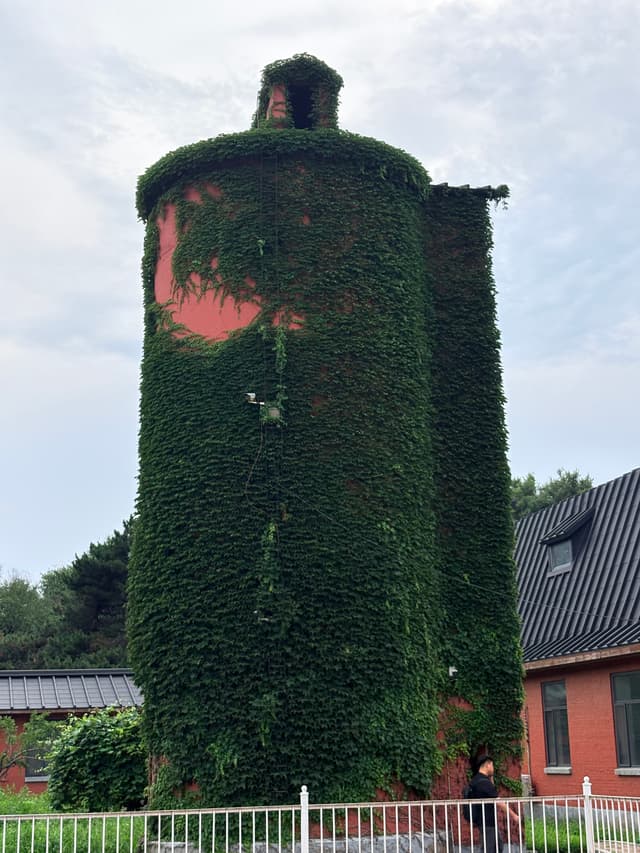 Ivy-covered cylindrical tower beside a red building and white fence