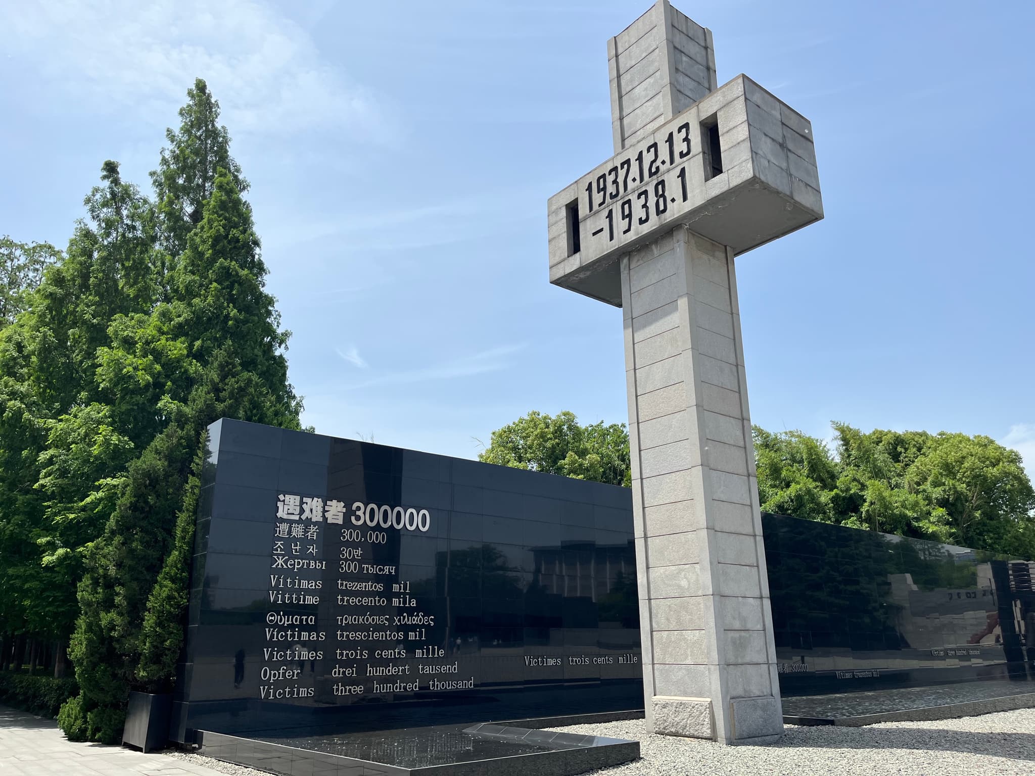 A tall concrete cross-shaped monument stands next to a black granite wall with inscribed text