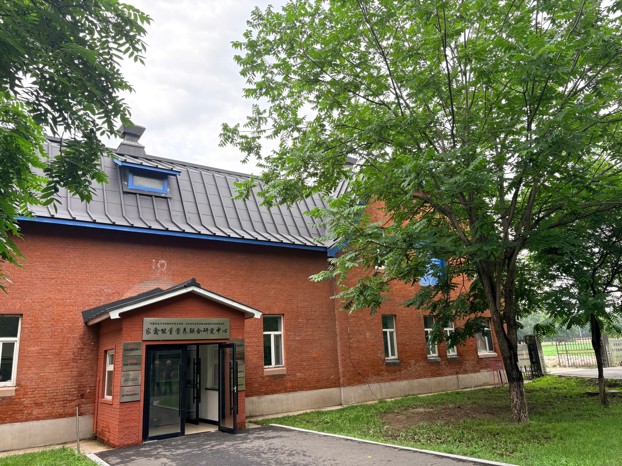 Red-brick building with a tiled roof, gated entrance, and mature trees