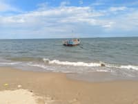 Small fishing boat floating offshore beyond gentle waves on a sandy beach