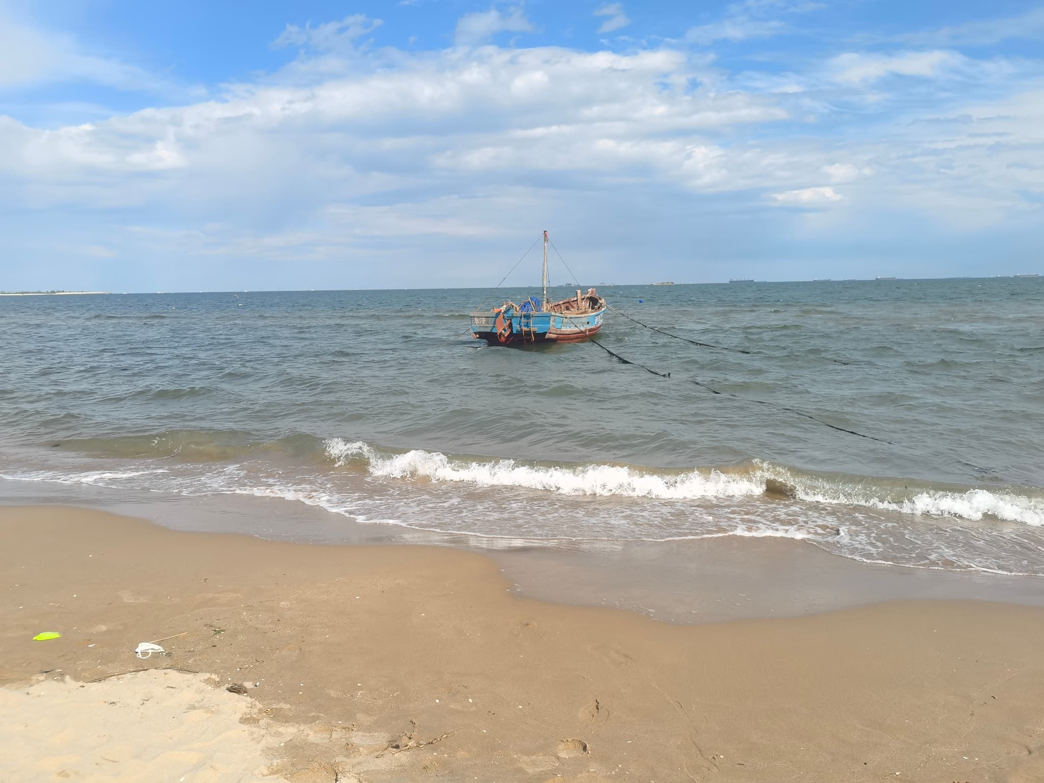 Small fishing boat floating offshore beyond gentle waves on a sandy beach