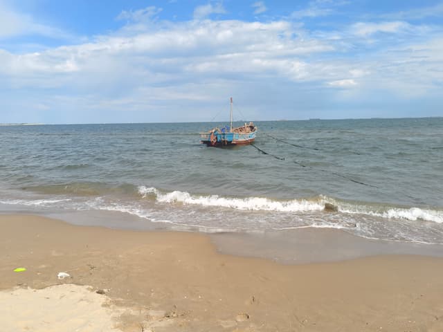 Small fishing boat floating offshore beyond gentle waves on a sandy beach