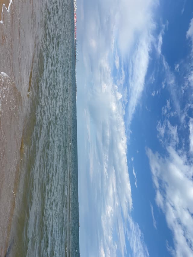 Cloud-dappled sky above a textured shoreline and open water