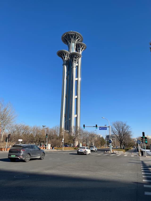 Three tall, slender towers with tree-like crowns rise against a clear blue sky above a street intersection