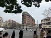 A street intersection with a distinctive triangular-shaped building, surrounded by other structures, trees, and people walking