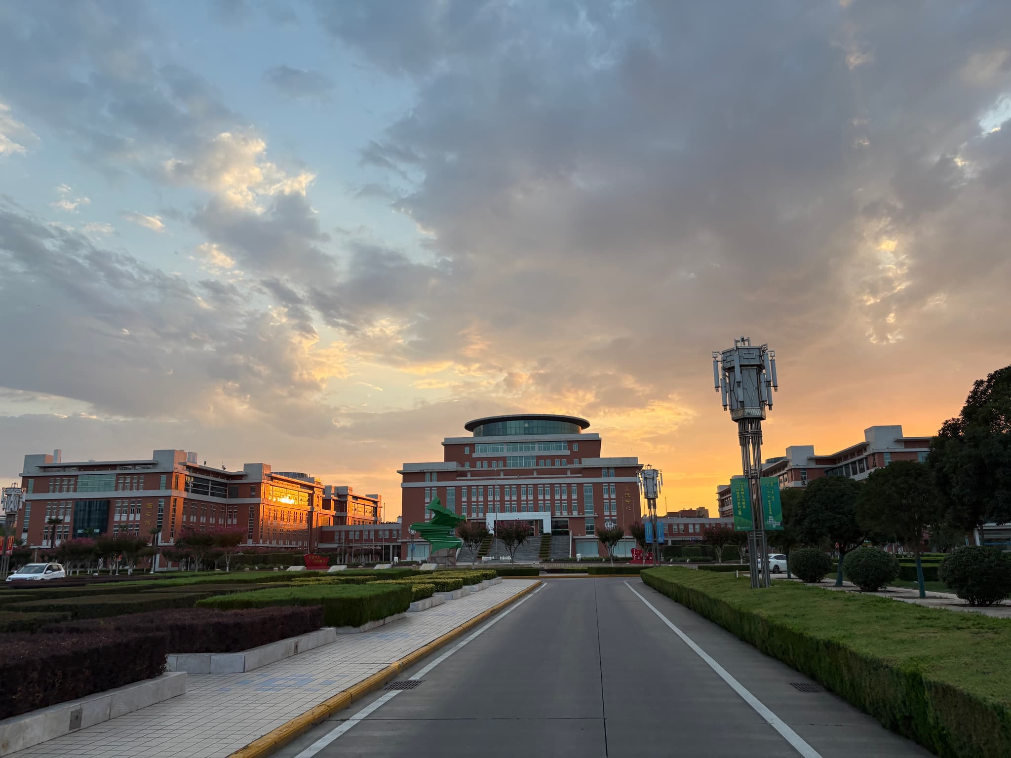 A wide view of a university campus during sunset, with modern buildings and manicured lawns under a dramatic sky