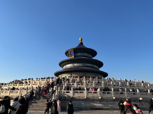The Temple of Heaven in Beijing, a circular, multi-tiered structure surrounded by a crowd of visitors under a clear blue sky