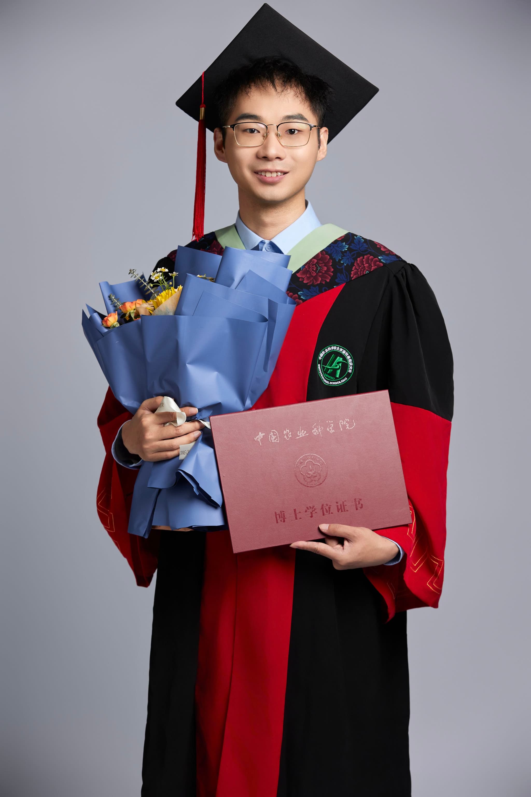 A person wearing a graduation cap and gown holds a bouquet of flowers and a diploma folder