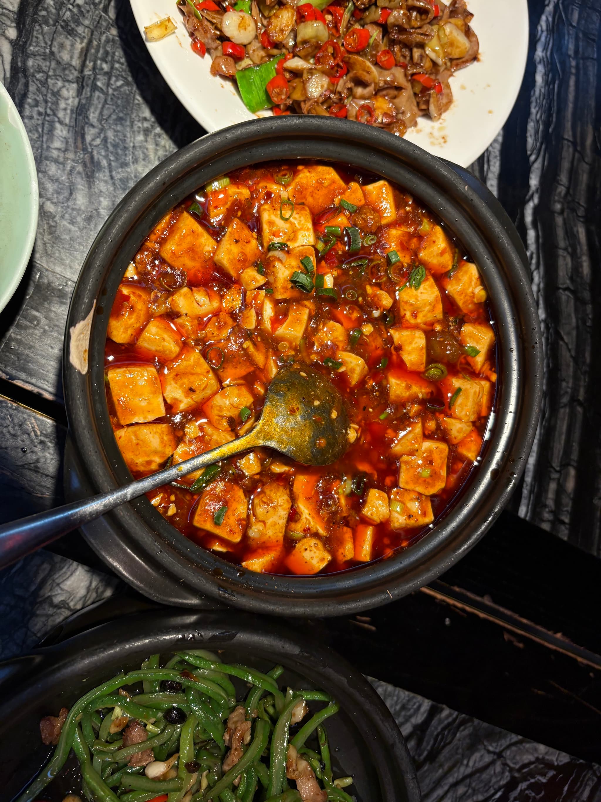 A black pot filled with spicy tofu stew, garnished with herbs and served with other dishes on a marble table