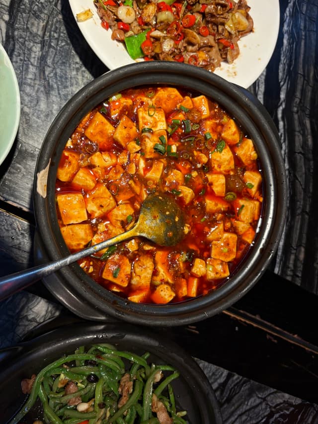 A black pot filled with spicy tofu stew, garnished with herbs and served with other dishes on a marble table