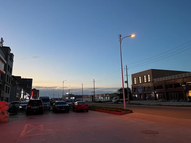 A quiet urban street at dusk with parked cars, streetlights, and buildings on either side