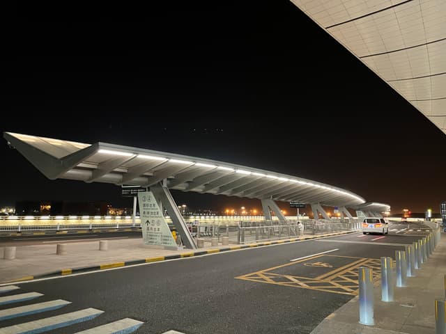 A modern, illuminated airport terminal at night with a sleek, angular design and empty surroundings