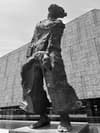 A towering, abstract sculpture stands in front of a modern, geometric building