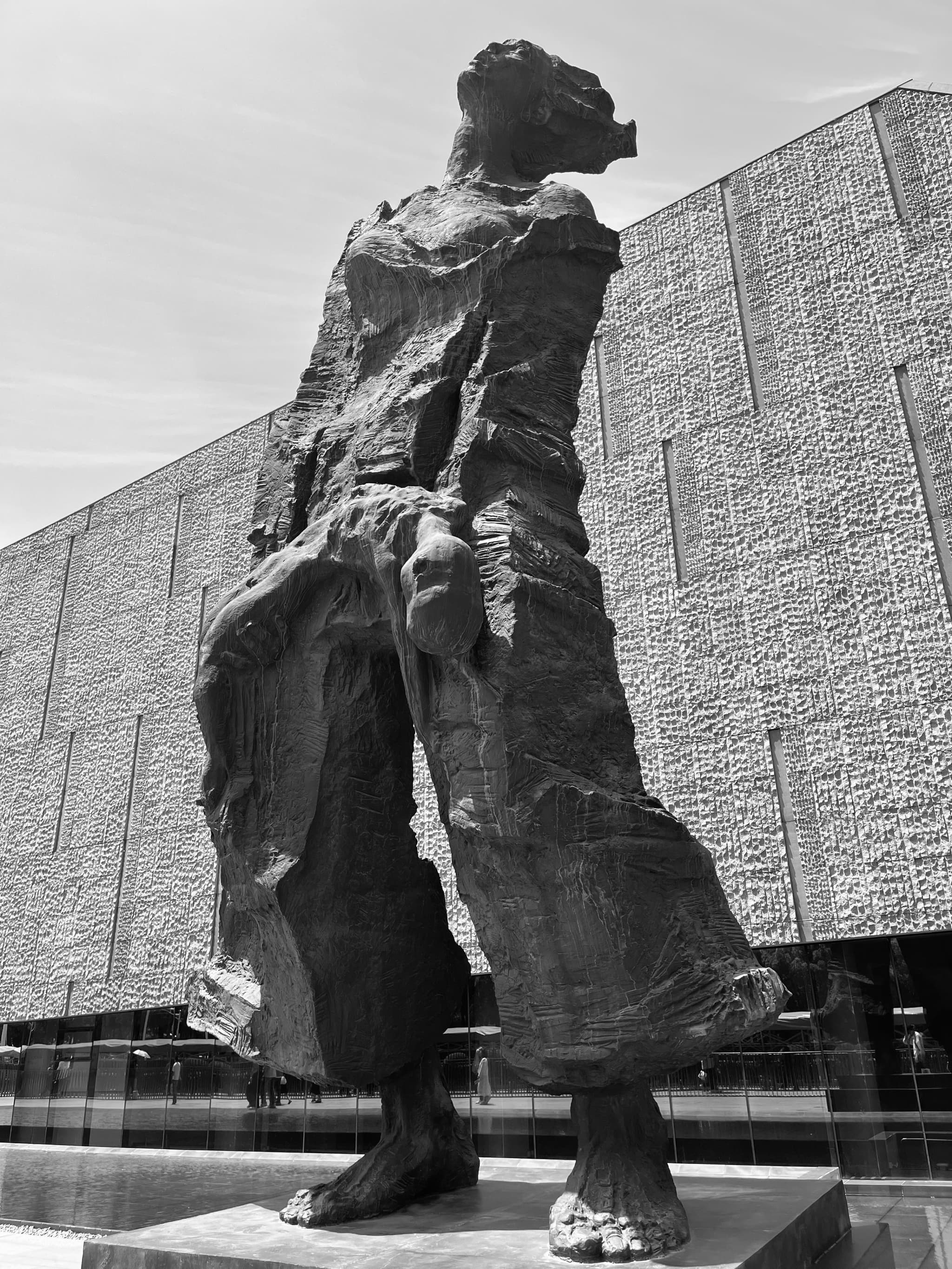 A towering, abstract sculpture stands in front of a modern, geometric building