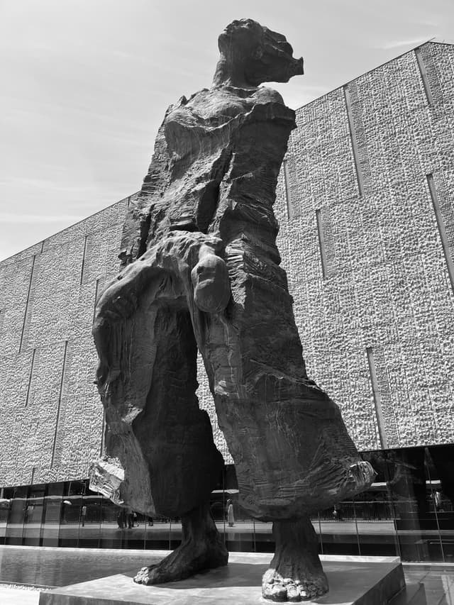 A towering, abstract sculpture stands in front of a modern, geometric building