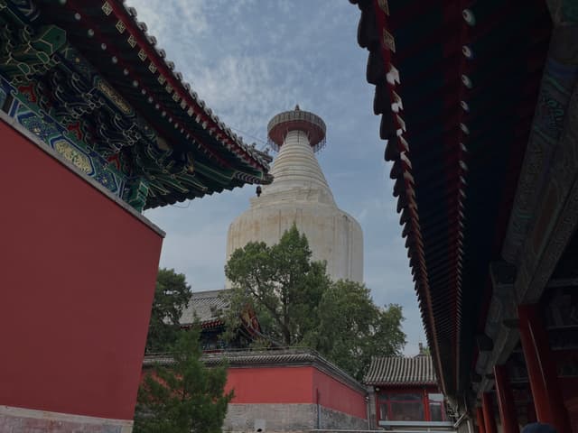 A white pagoda surrounded by traditional Chinese architecture and red walls under a partly cloudy sky