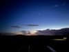 A serene twilight sky with a bright star or planet visible, silhouetted clouds, and faintly illuminated ground features
