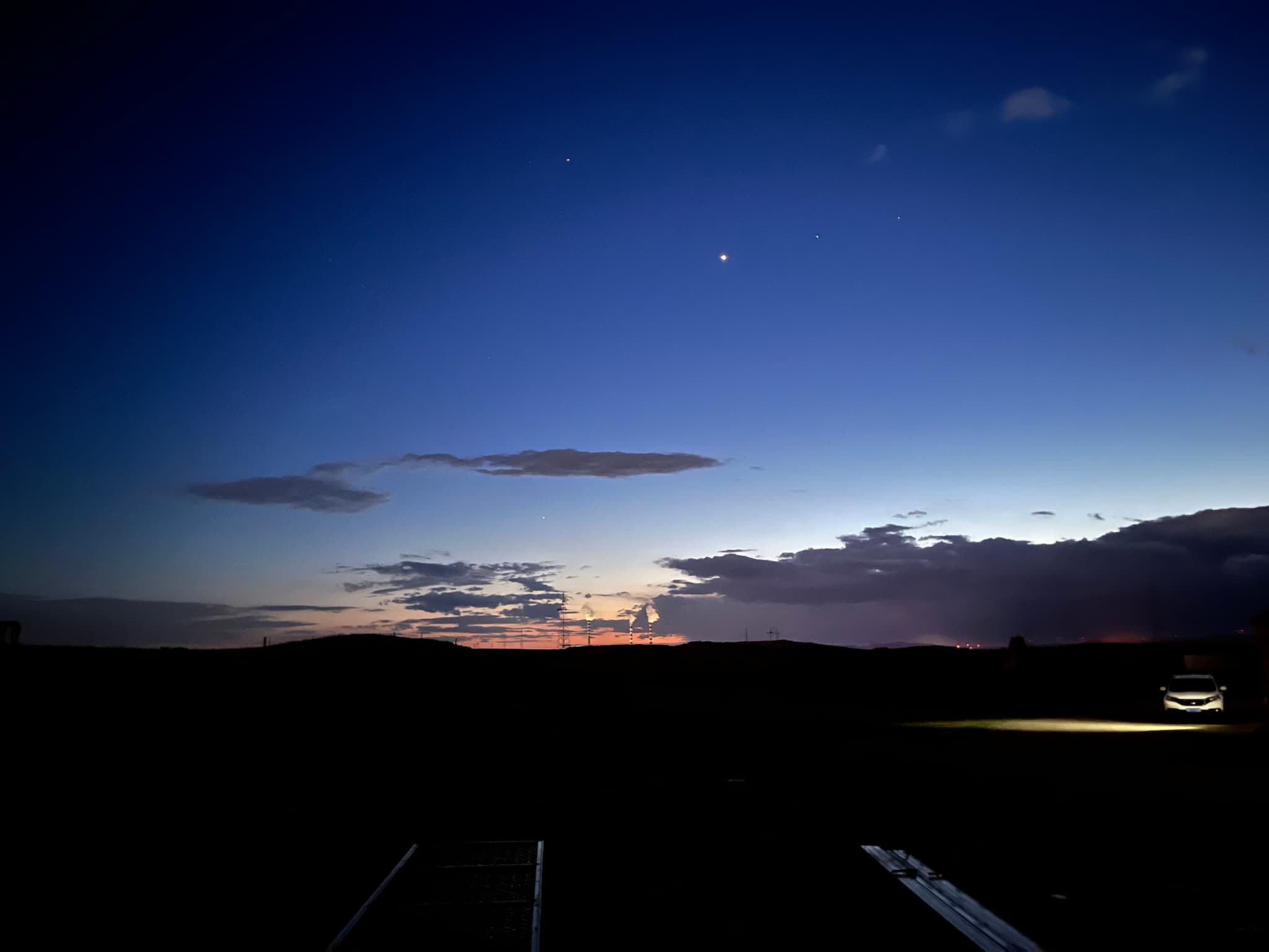 A serene twilight sky with a bright star or planet visible, silhouetted clouds, and faintly illuminated ground features