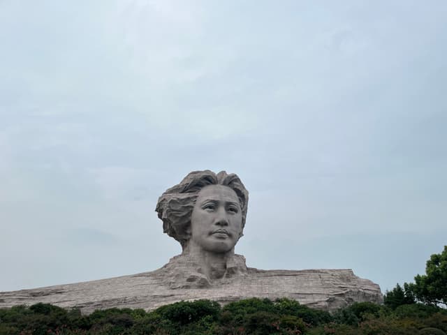 A rock formation resembling a human profile set against a cloudy sky, surrounded by sparse vegetation